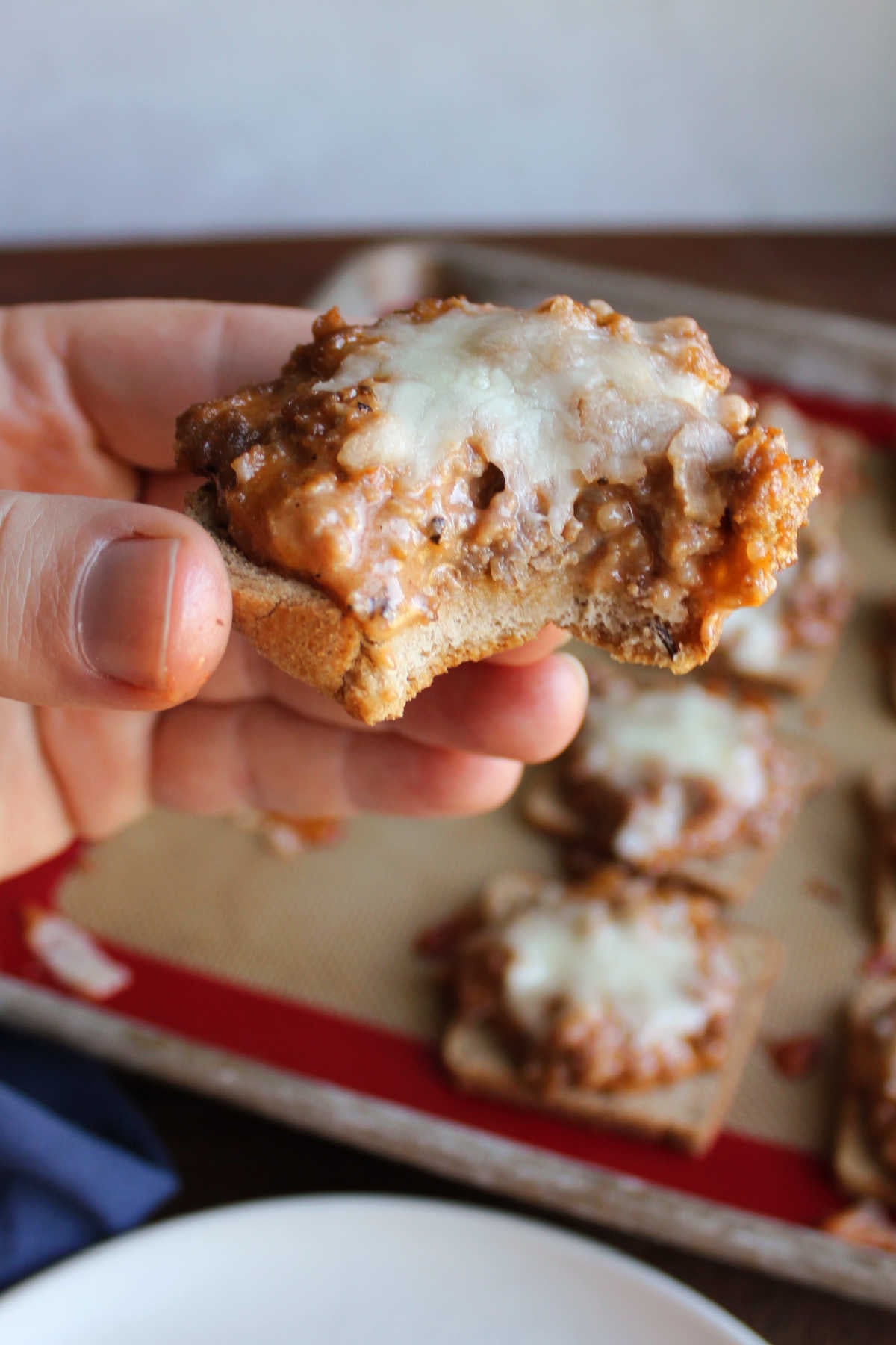 Jeff's Pizza Bites 11 Hand holding a pizza snack with a bite missing showing the cheesy and saucy sausage mixture on top of a piece of cocktail rye bread with melted mozzarella cheese on top.