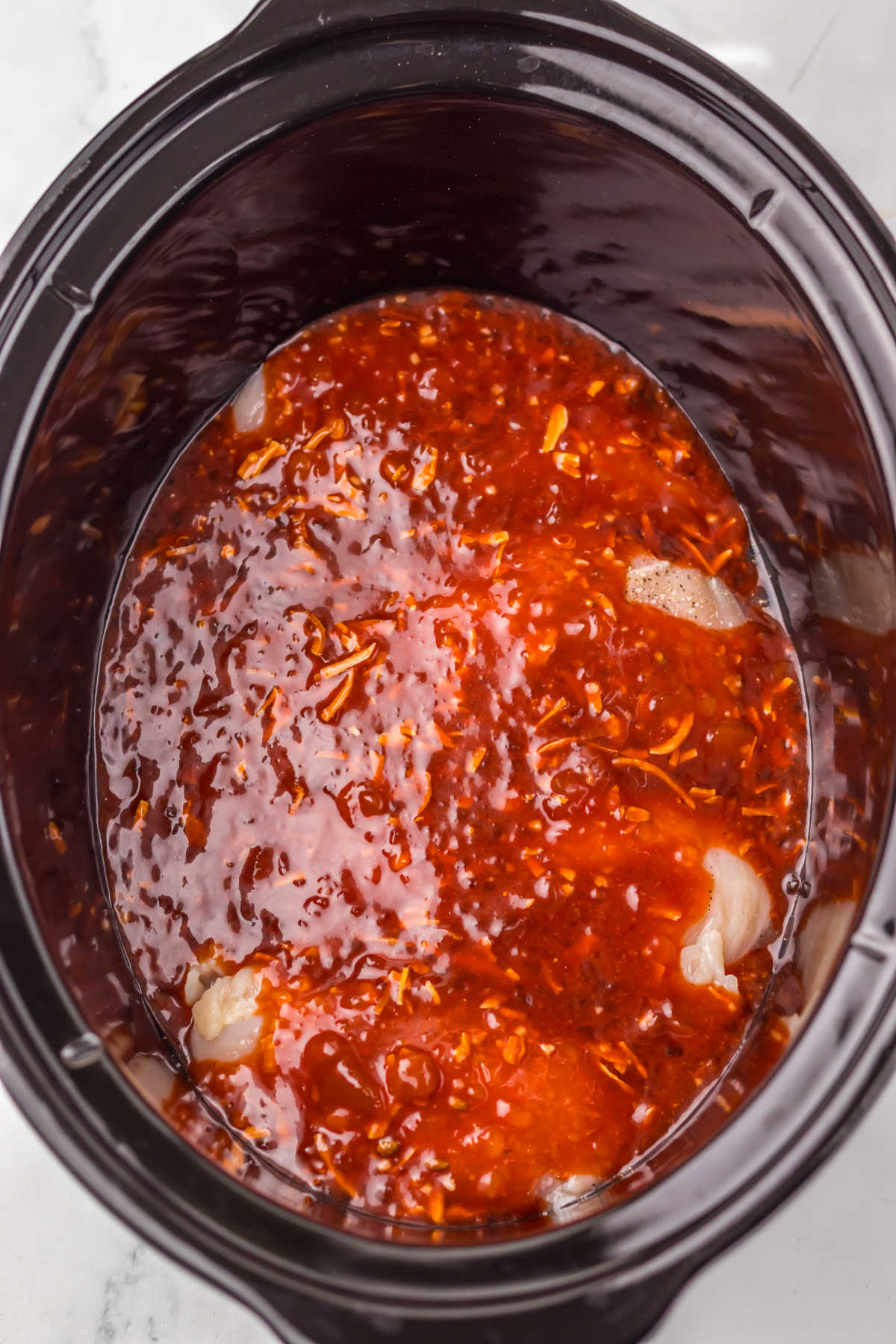 Crockpot filled with chicken breasts and sauce made from catalina dressing, apricot jam and seasonings, ready to cook. 