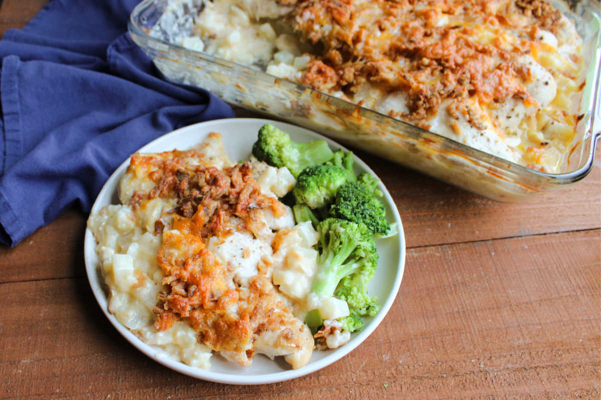 Cheesy Chicken and Potato Casserole 7 Plate filled with cheesy chicken and hash brown casserole topped with browned french fried onions and cheese served with broccoli, ready to eat.