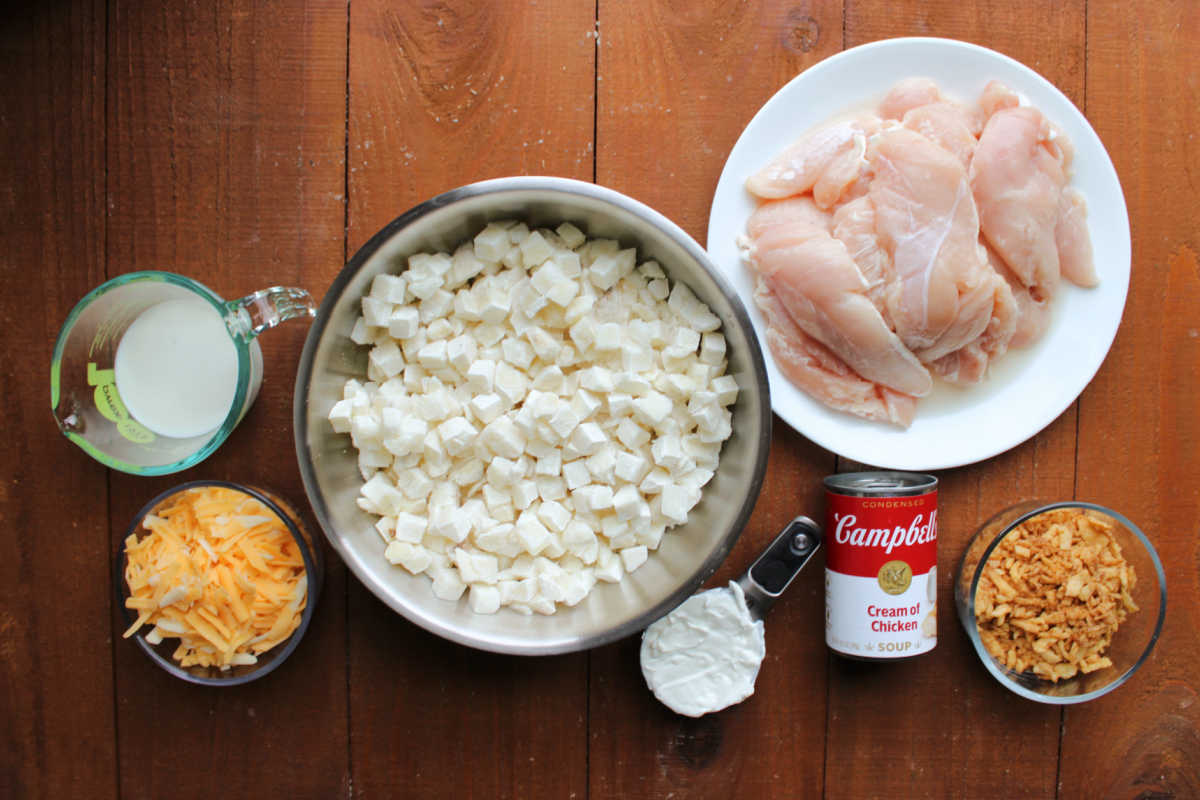Cheesy Chicken and Potato Casserole 6 Ingredients including shredded cheddar cheese, milk, frozen hash browns, sour cream, cream of chicken soup, chicken tenderloins, and french fried onions ready to be made into a casserole.