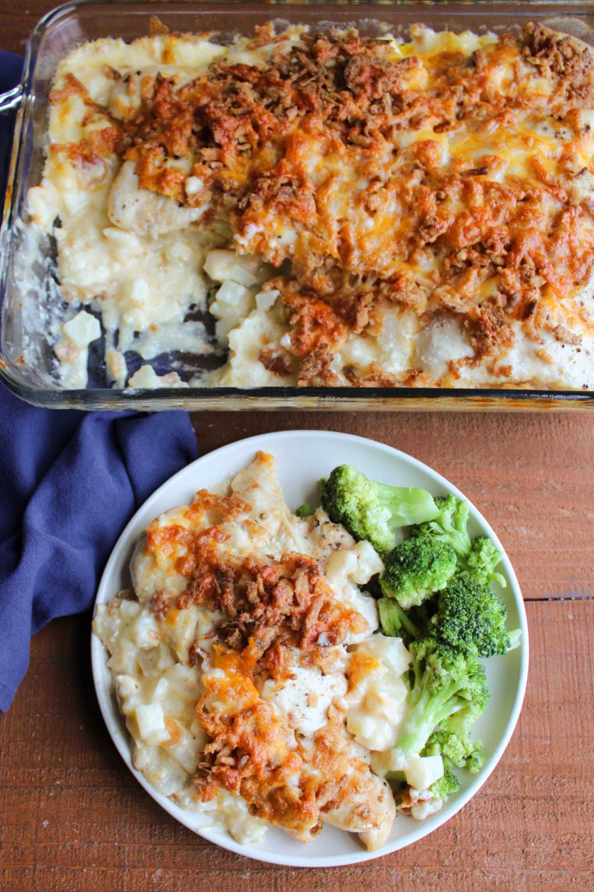 Cheesy Chicken and Potato Casserole 8 Casserole dish filled with creamy hash brown mixture topped with pieces of chicken, browned french fried onions and cheese next to a plate with a serving of the casserole served with broccoli.