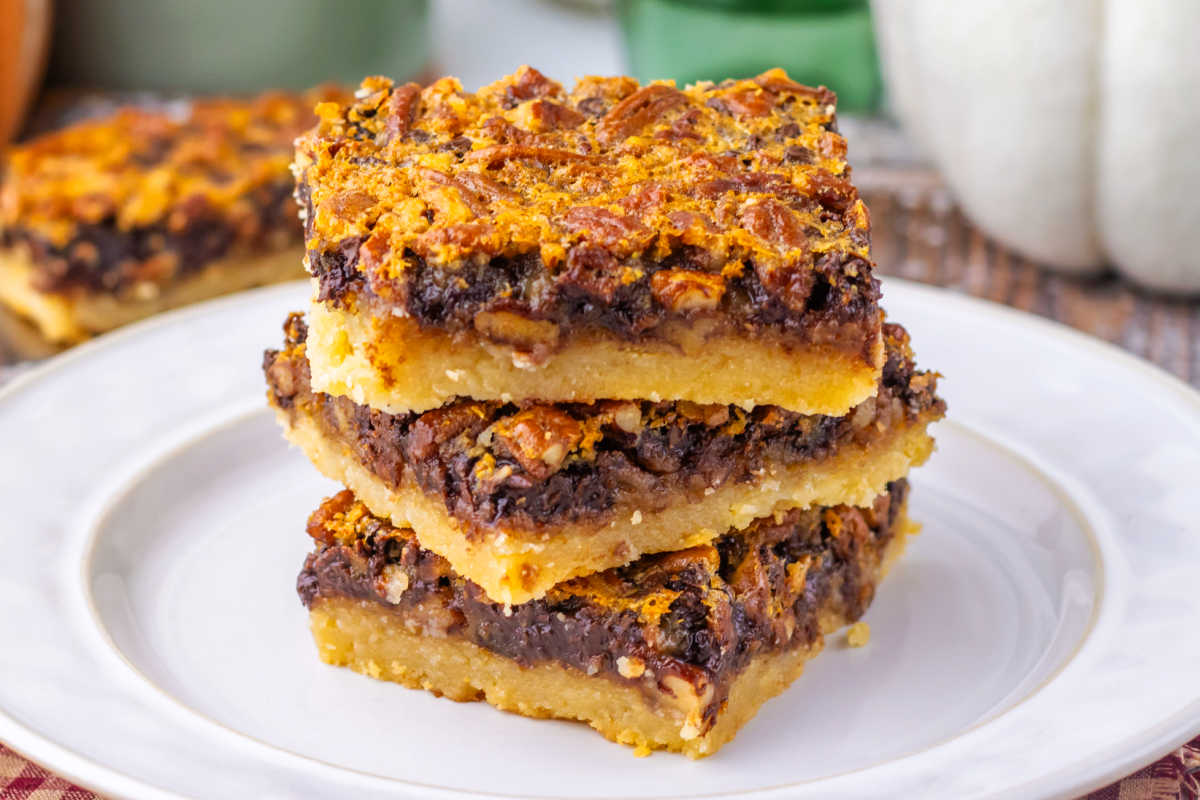 Stack of chocolate pecan pie bars with cookie crust and chocolaty pecan filling, ready to eat. 