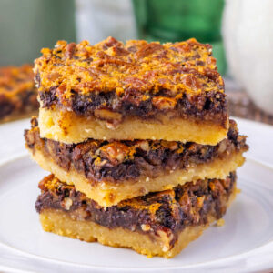 Stack of square pieces of chocolate pecan pie bars with shortbread crust topped with gooey chocolate filling and lots of pecan pieces.