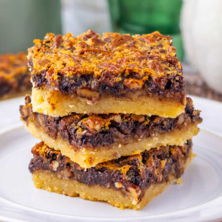 Chocolate Pecan Pie Bars 1 Stack of square pieces of chocolate pecan pie bars with shortbread crust topped with gooey chocolate filling and lots of pecan pieces.