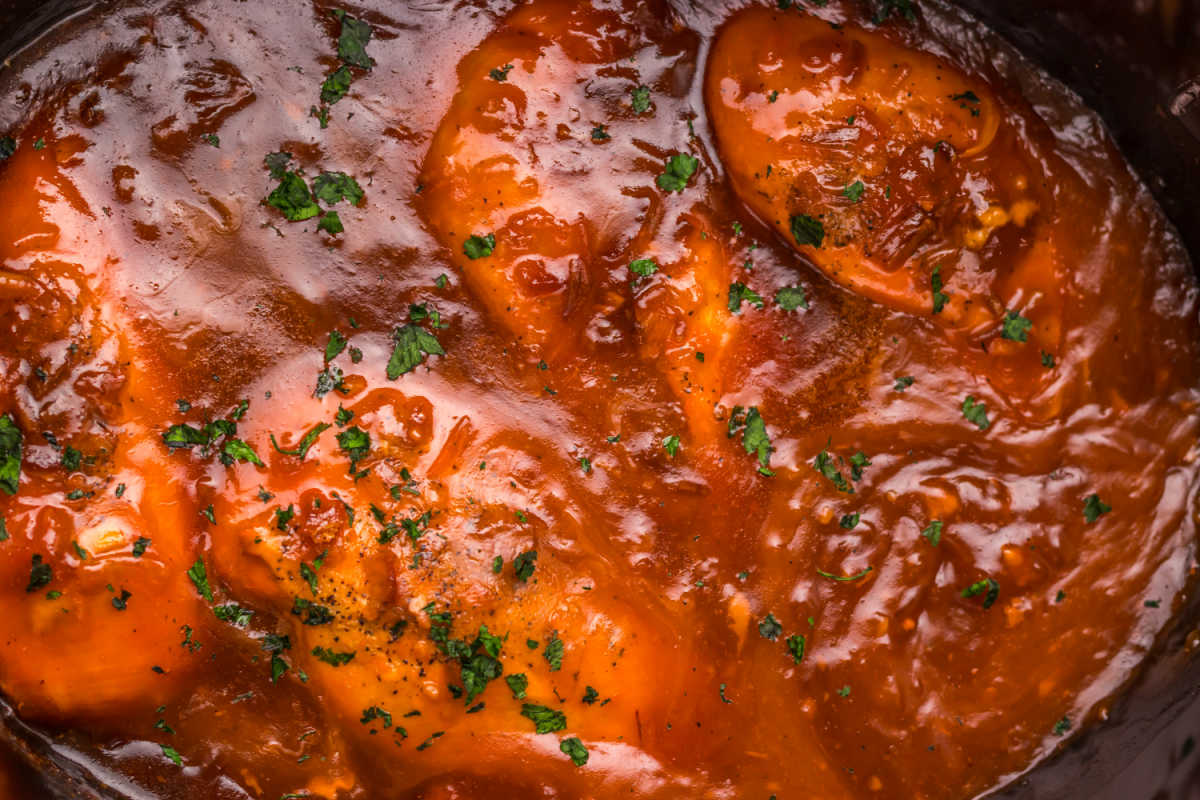 Crockpot filled with cooked chicken breasts in thickened red sauce made from catalina dressing, apricot jam and seasonings. 