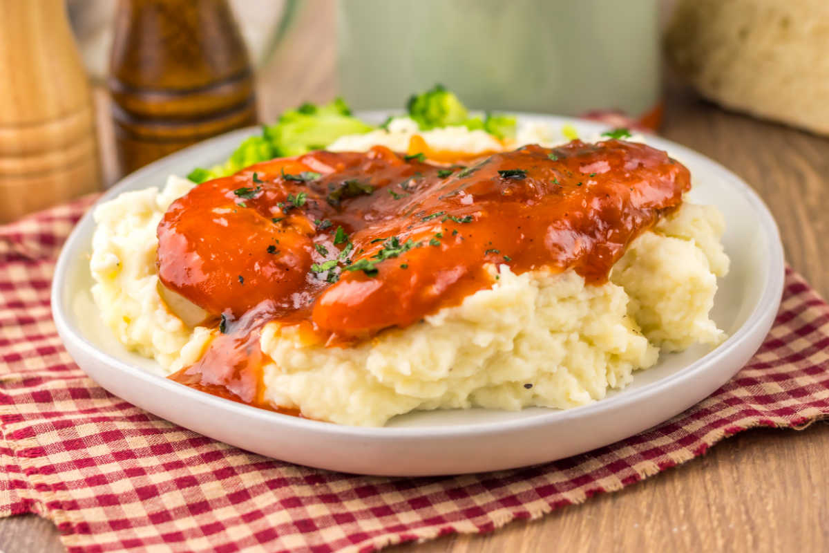 Dinner plate topped with a pile of mashed potatoes topped with chicken breasts in red catalina sauce and chopped parsley. 