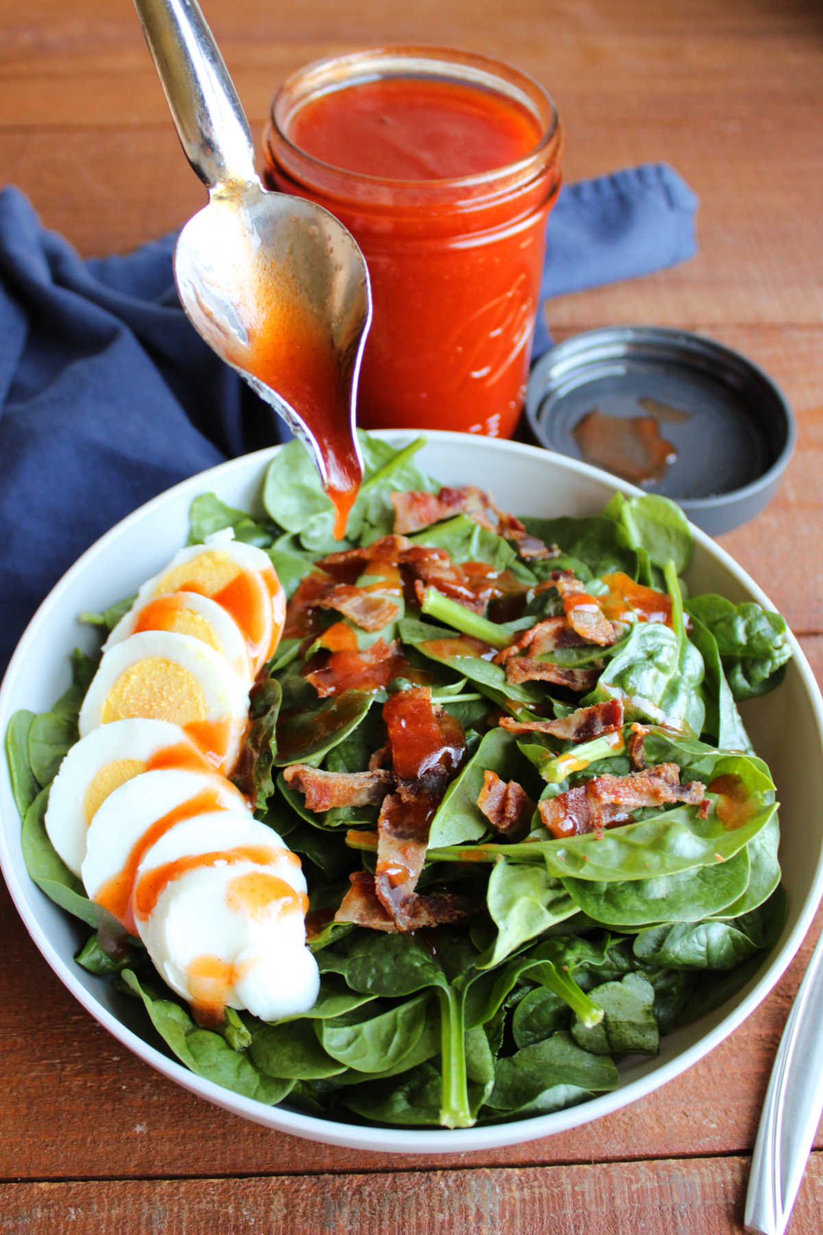 Drizzle spoon distributing homemade catalina salad dressing over a salad with bacon and hard boiled egg. 