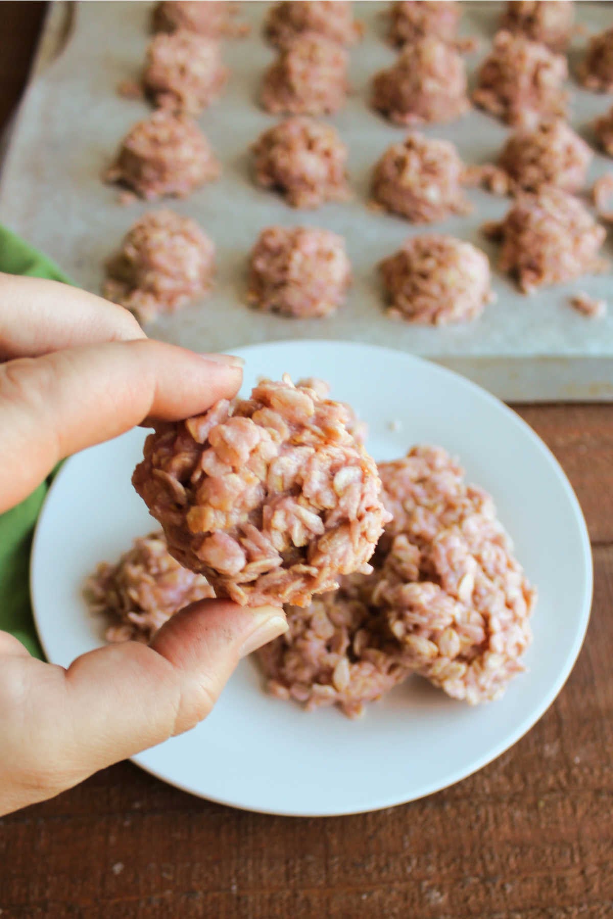 Hand holding a pink no bake cookie with lots of oats and a mixture made from butter, sugar, strawberry milk powder, and milk. 