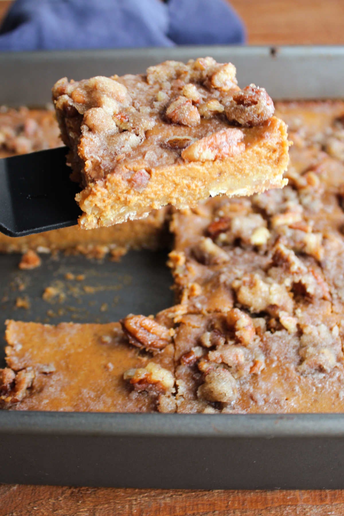 Grandma's Pumpkin Pie Bars 8 Spatula lifting a pumpkin pie bar out of the pan showing the brown sugar oat crust, creamy pumpkin pie filling, and pecan topping.
