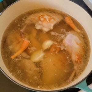 Pot with browned pieces of rabbit, carrots, and onion being made into stock.