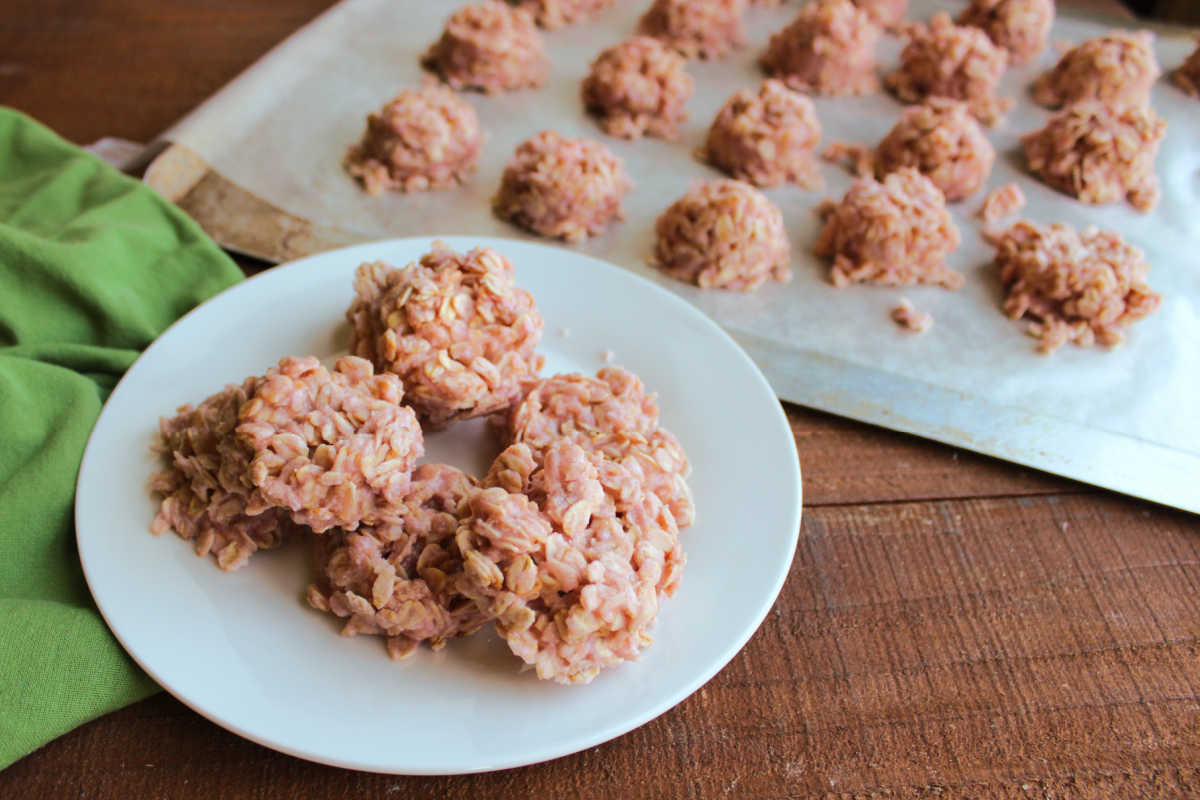 Plate of strawberry milk no bake cookies next to a cookie sheet with more cookies nearby. 