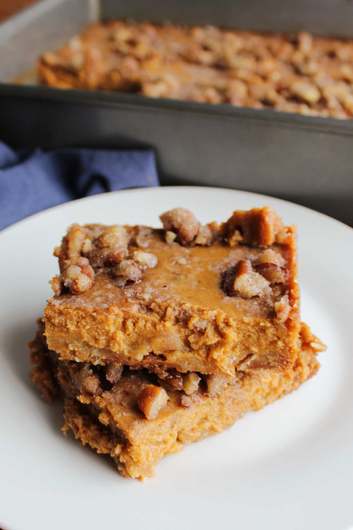 Grandma's Pumpkin Pie Bars 9 Two pumpkin pie squares stacked on top of each other with the 9x13-inch pan they were baked in nearby.