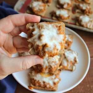 Jeff's Pizza Bites 13 Hand holding a pizza bite with cheesy sausage and pizza sauce mixture on a square of cocktail rye bread, ready to eat.