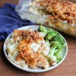 Dinner plate with helping of casserole with creamy hash brown mixture topped with pieces of chicken topped with browned cheese and french fried onions served with steamed broccoli, ready to eat..