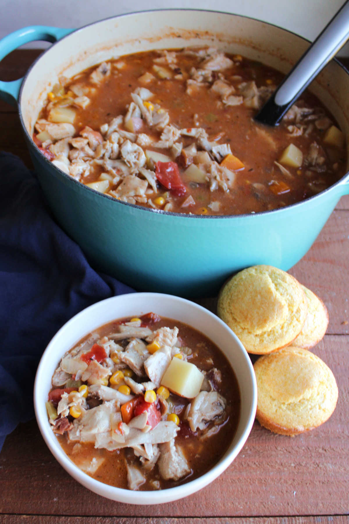 Bowl of southern rabbit stew served with corn  muffins next to the pot with more stew inside. 