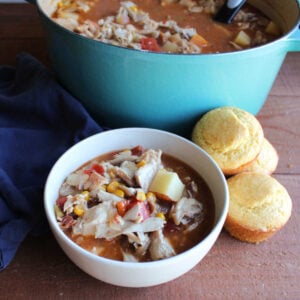 Bowl of rabbit stew with potatoes, carrots, and celery in a tomato and BBQ broth served with homemade corn muffins.