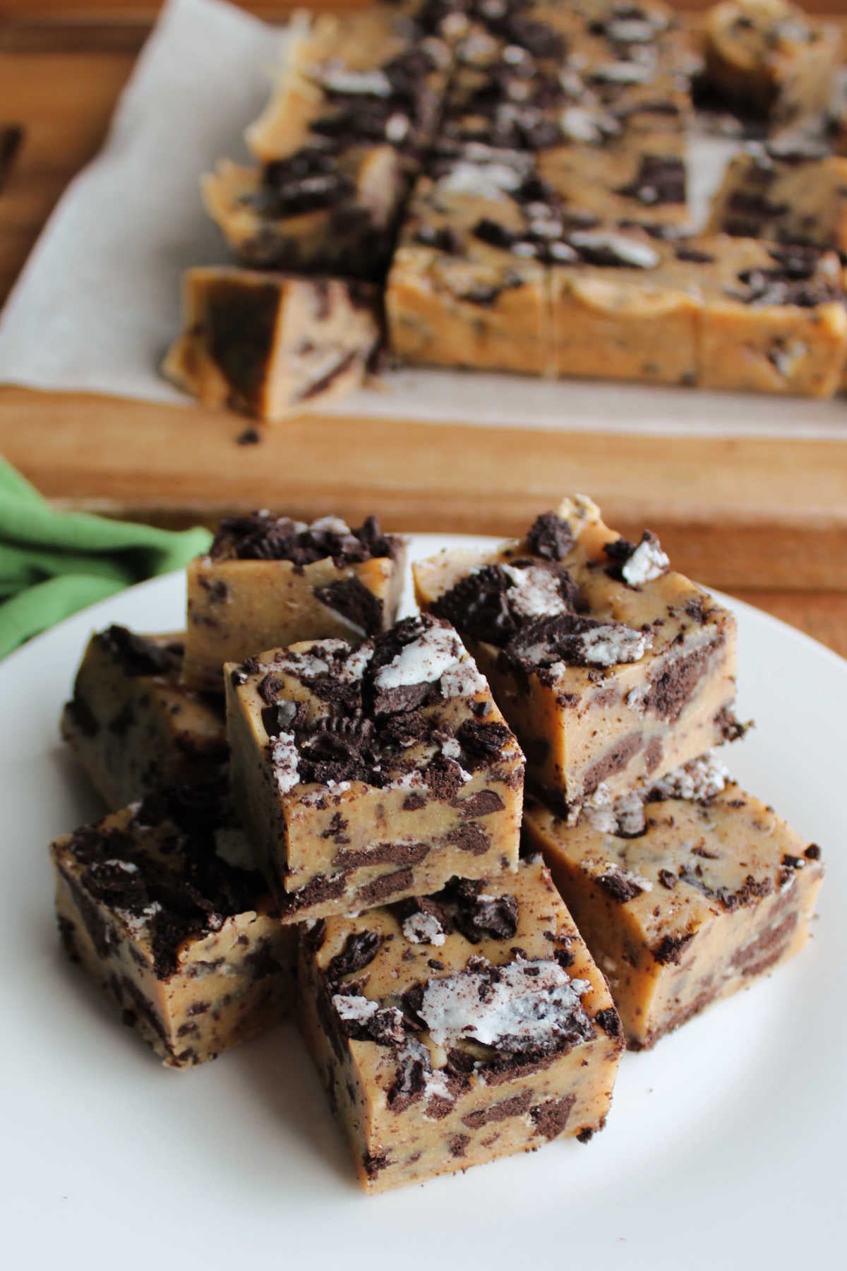 Plate filled with squares of peanut butter Oreo fudge in front of cutting board with the rest of the fudge on it. 
