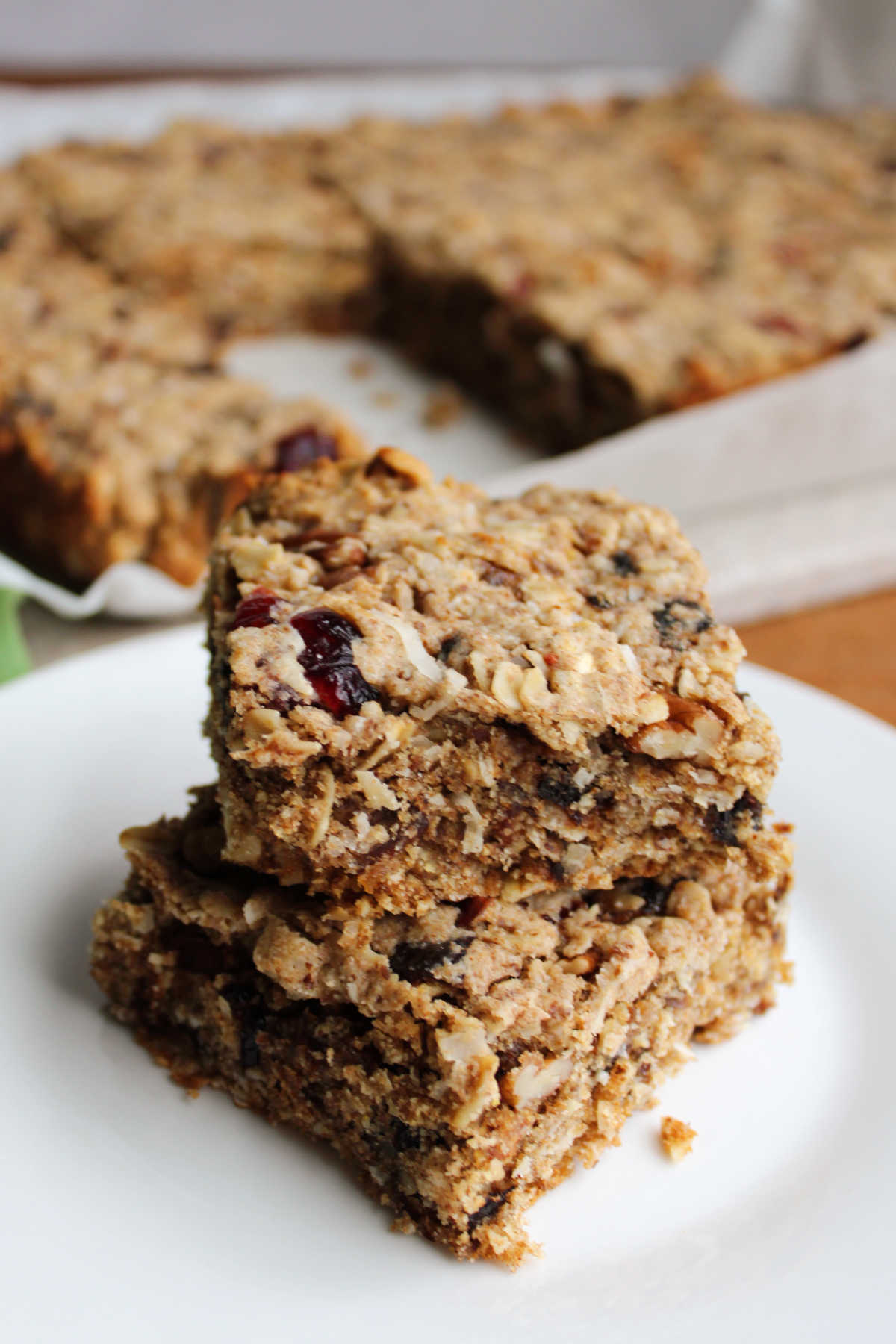 Squares of trail mix bars on plate showing chewy texture and loads of fruits and nuts inside. 