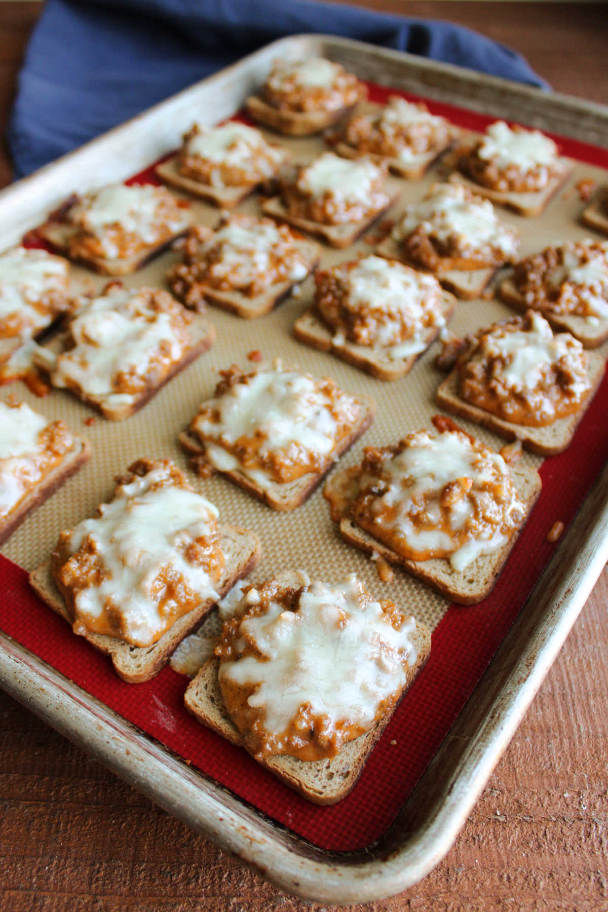 Jeff's Pizza Bites 8 Tray of baked pizza bites built on squares of cocktail rye bread topped with pizza sauce and sausage mixture and melted mozzarella cheese.